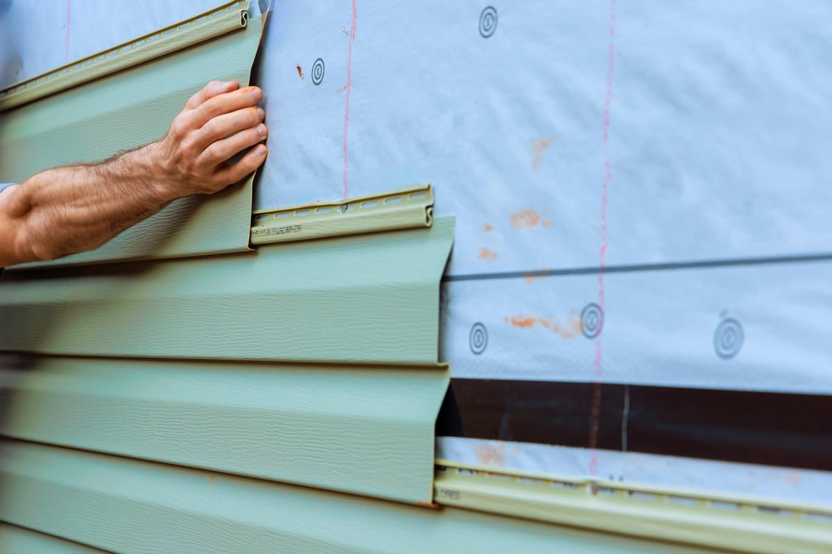 Construction worker carefully fitting green PVC siding onto wall during professional home improvement installation