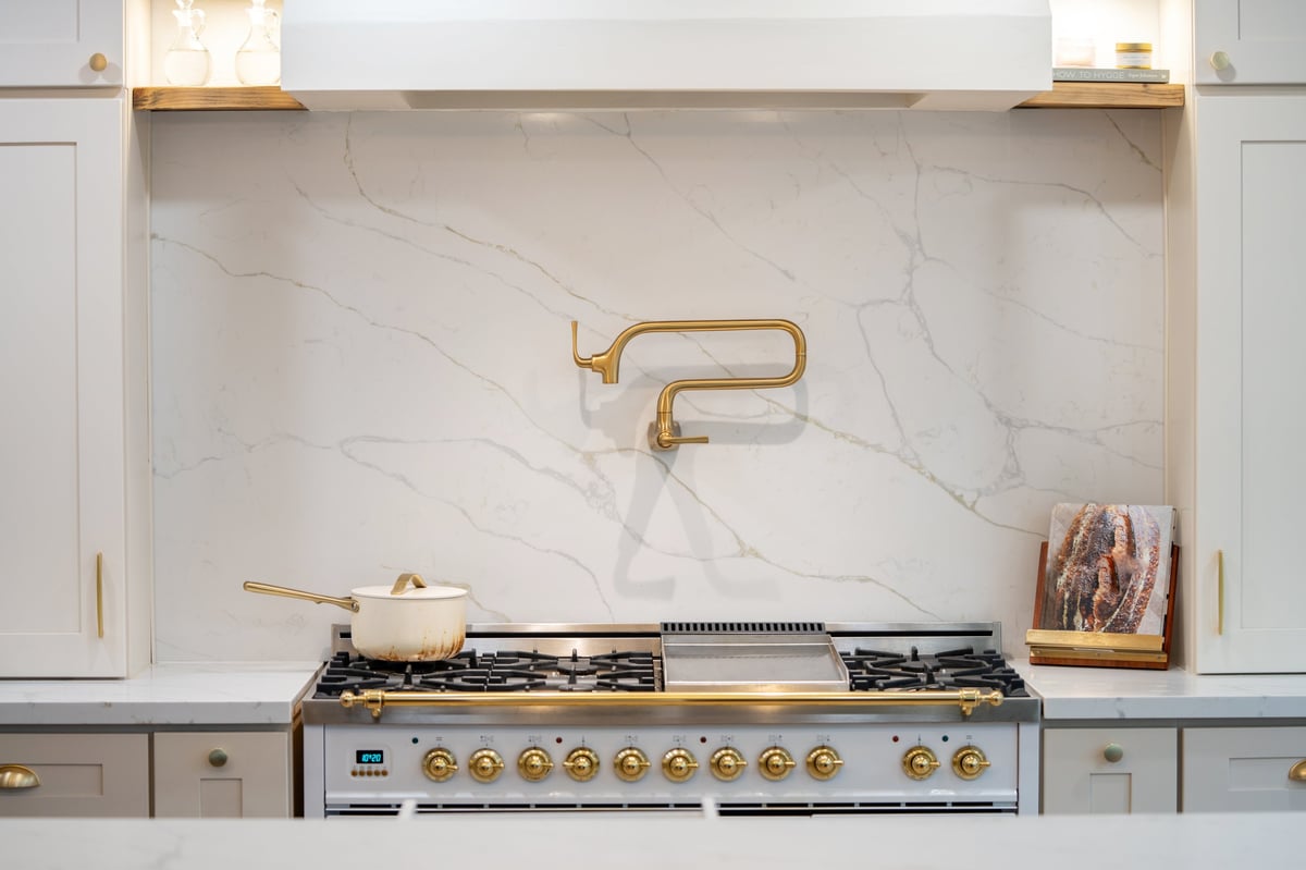 Bright modern kitchen interior with cream cabinetry, marble backsplash, gas range and brass fixtures in a clean contemporary home.